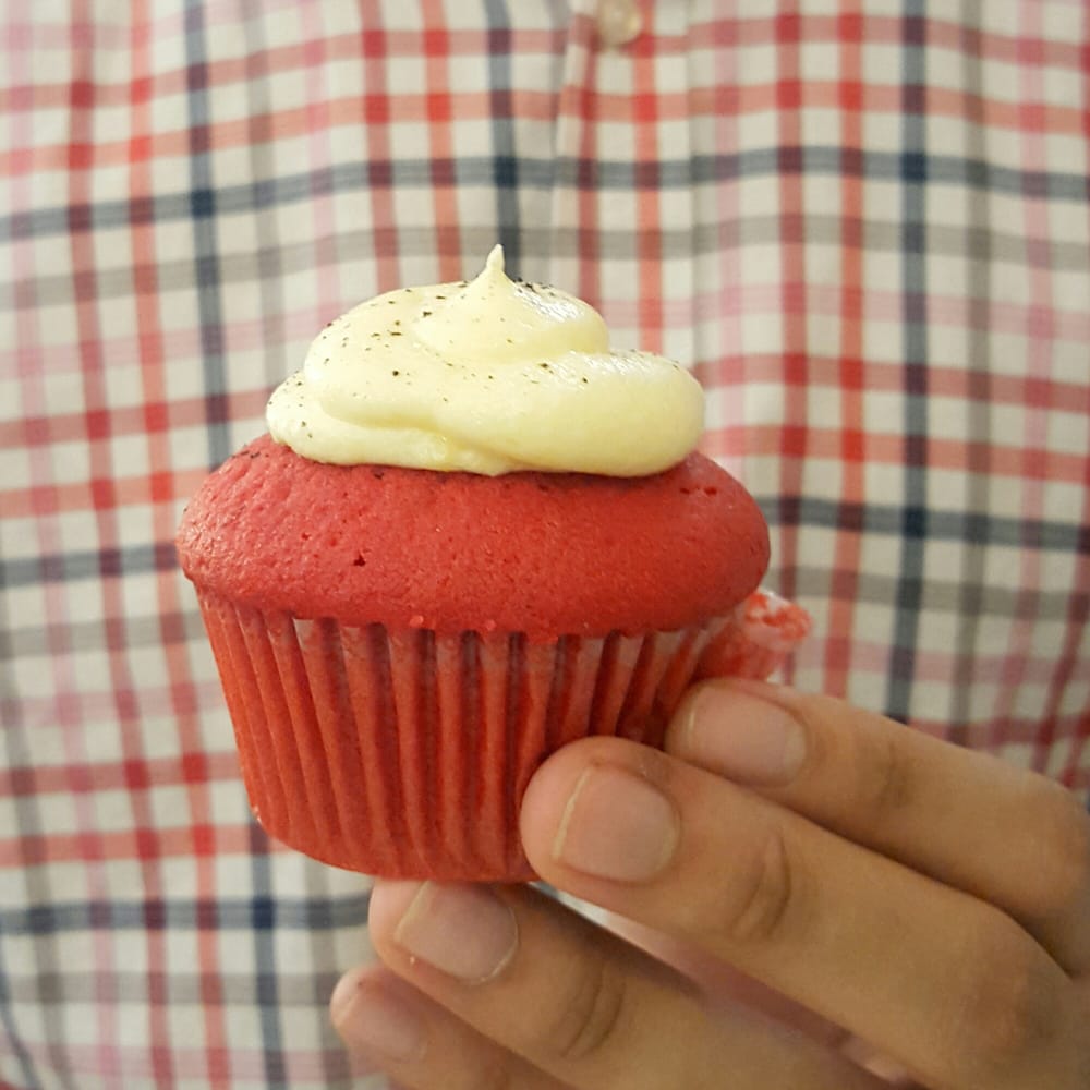 Red velvet cupcake with cream cheese frosting held in hand